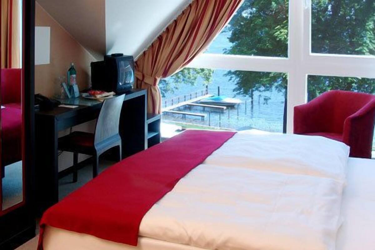 A hotel room with a bed, a desk, a chair, and a window with a view of trees.