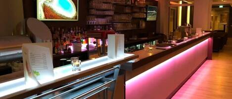 A bar area with a long counter, shelves with bottles, and a menu stand.