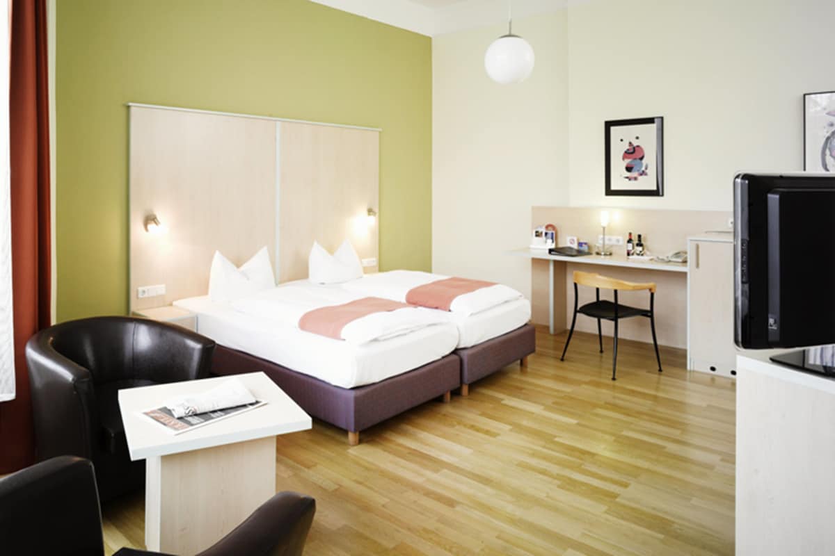 A hotel room with a bed, a desk, a chair, and a television.