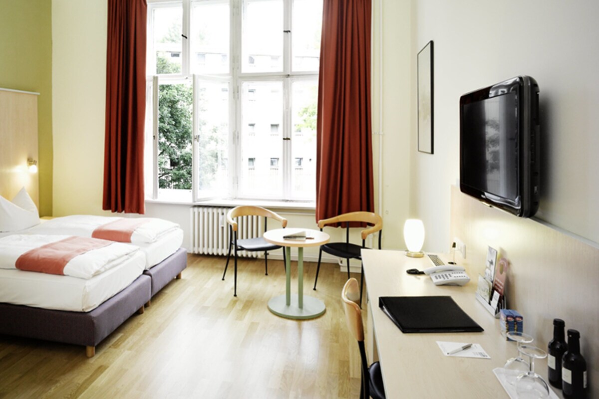 A hotel room with a bed, a desk, a chair, a TV, and a window with curtains.