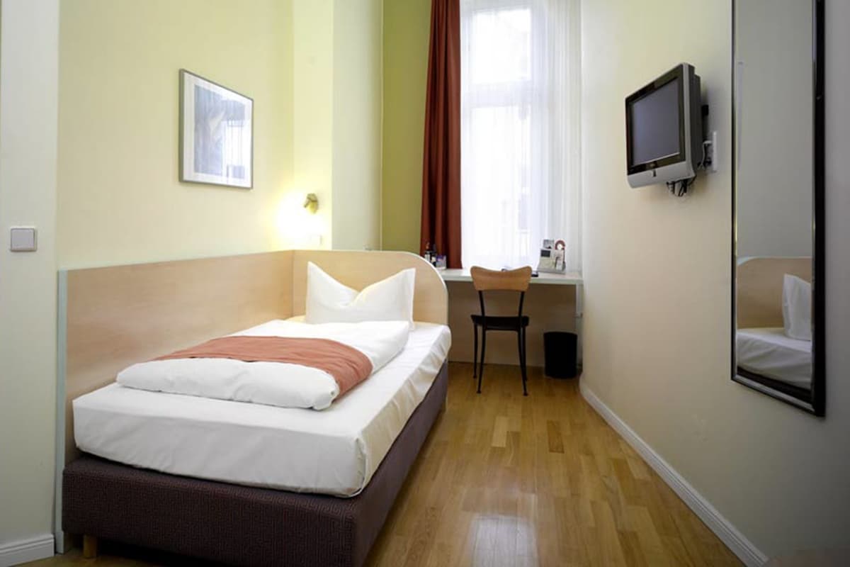 A hotel room with a bed, a desk, a chair, a television, and a window with curtains.