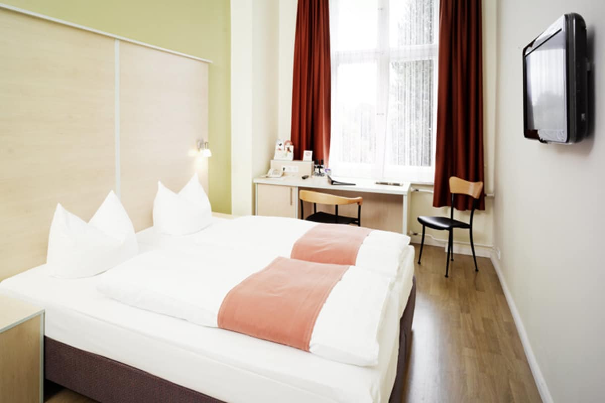 A hotel room with a large bed, a desk, and a TV mounted on the wall.
