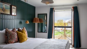 Un dormitorio con cama, dos lámparas de pared, una ventana con cortinas y vistas a un jardín.