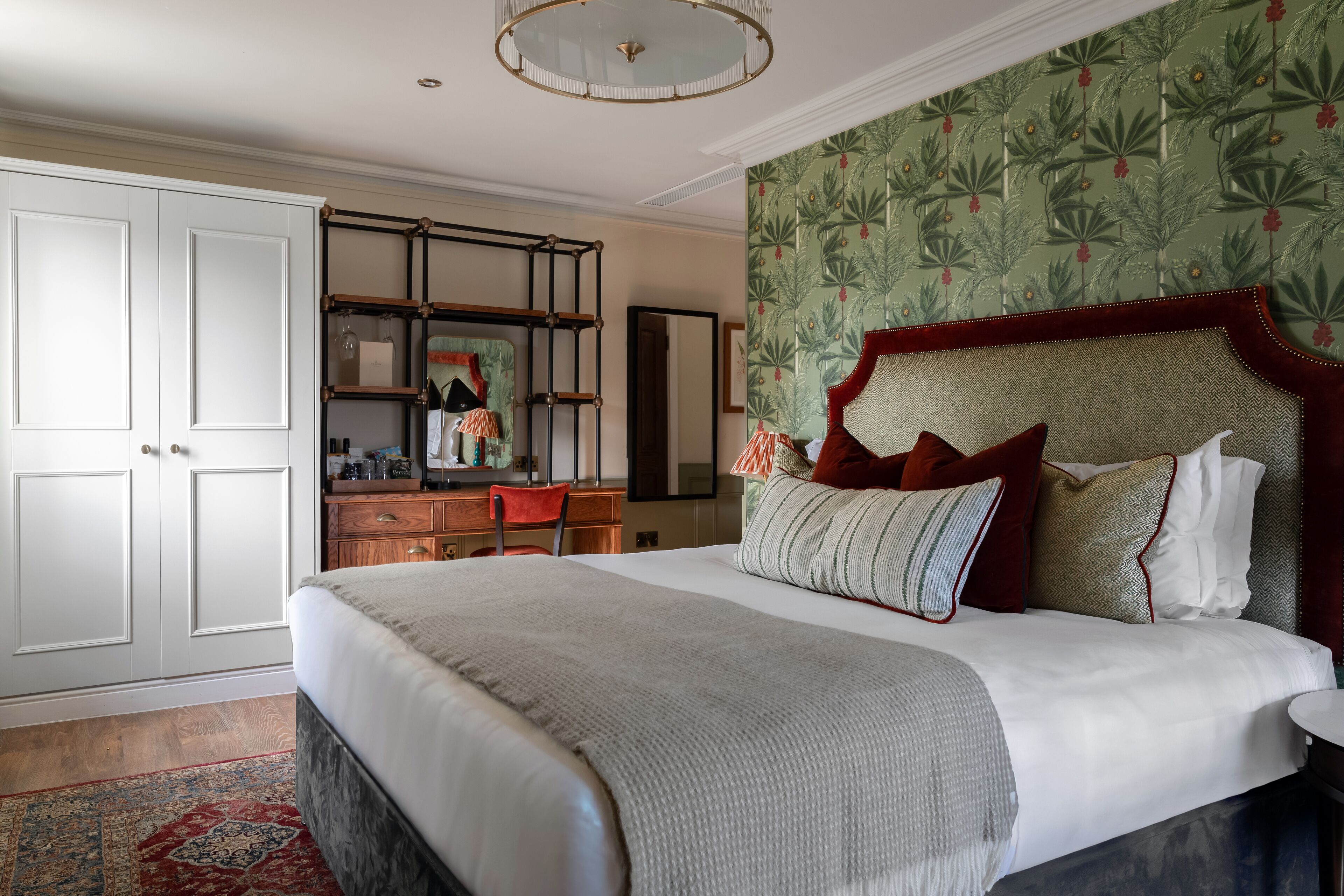 A bedroom with a large bed, a dresser, a mirror, and a wardrobe.