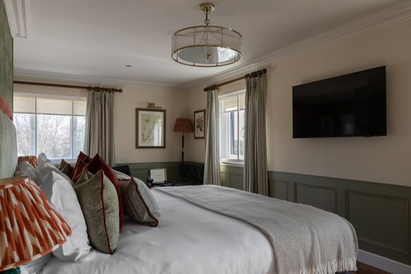 A hotel room with a large bed, a flat-screen TV, a desk with a lamp, and a window with curtains.