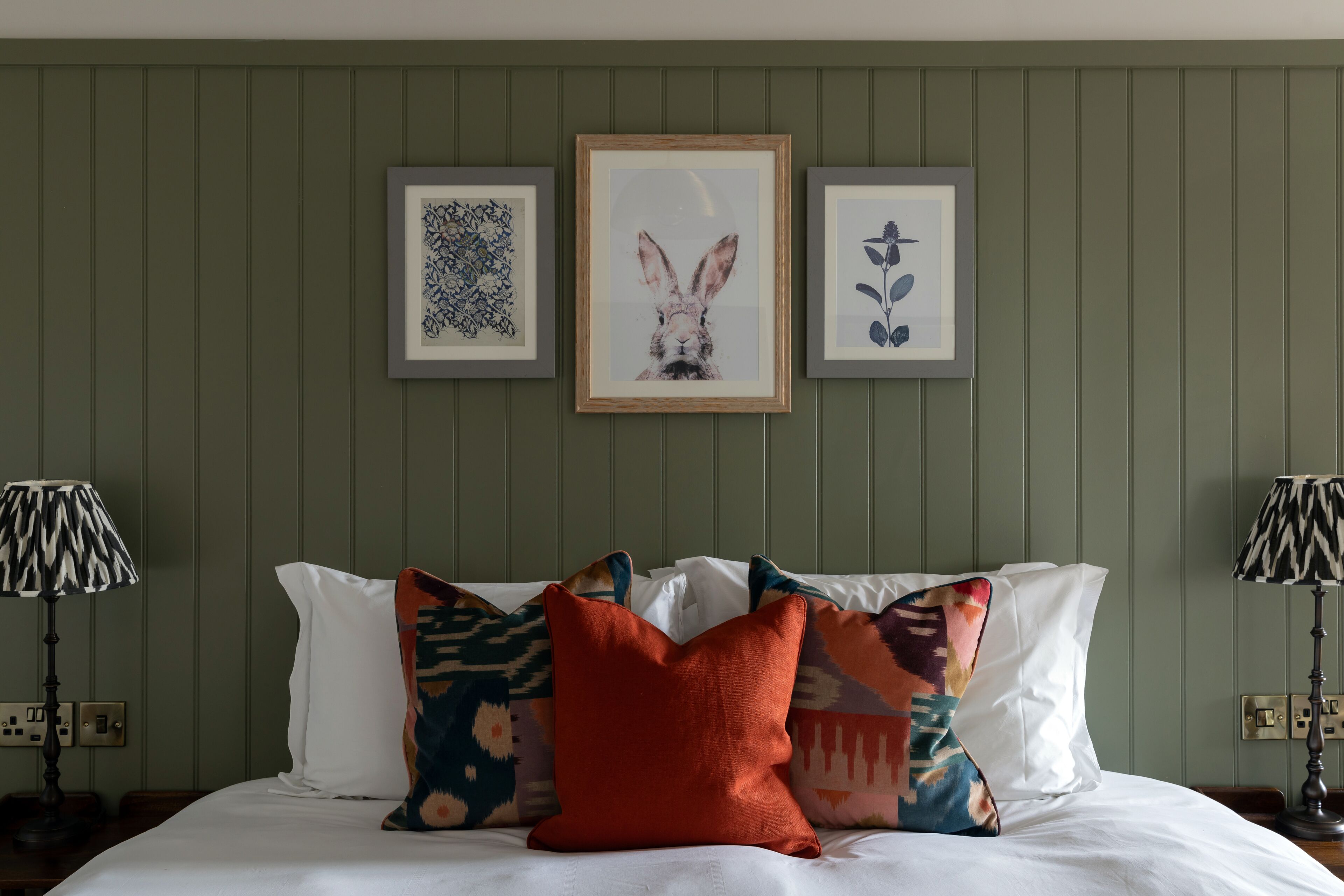 A neatly made bed with patterned pillows, framed artwork on the wall, and two lamps on either side.