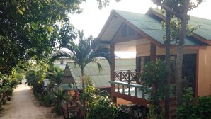 Un sentier mène à un bungalow doté d’un toit végétalisé, entouré d’une végétation luxuriante et d’un petit jardin.