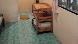 Une petite pièce avec une table en bois, une fenêtre avec un rideau et un sol carrelé.