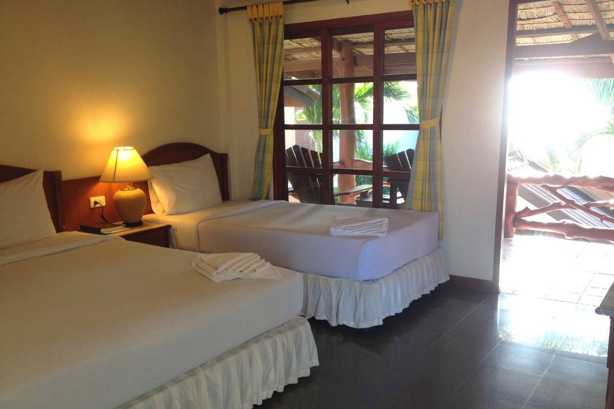A hotel room with two beds, a nightstand with a lamp, and a window with curtains.