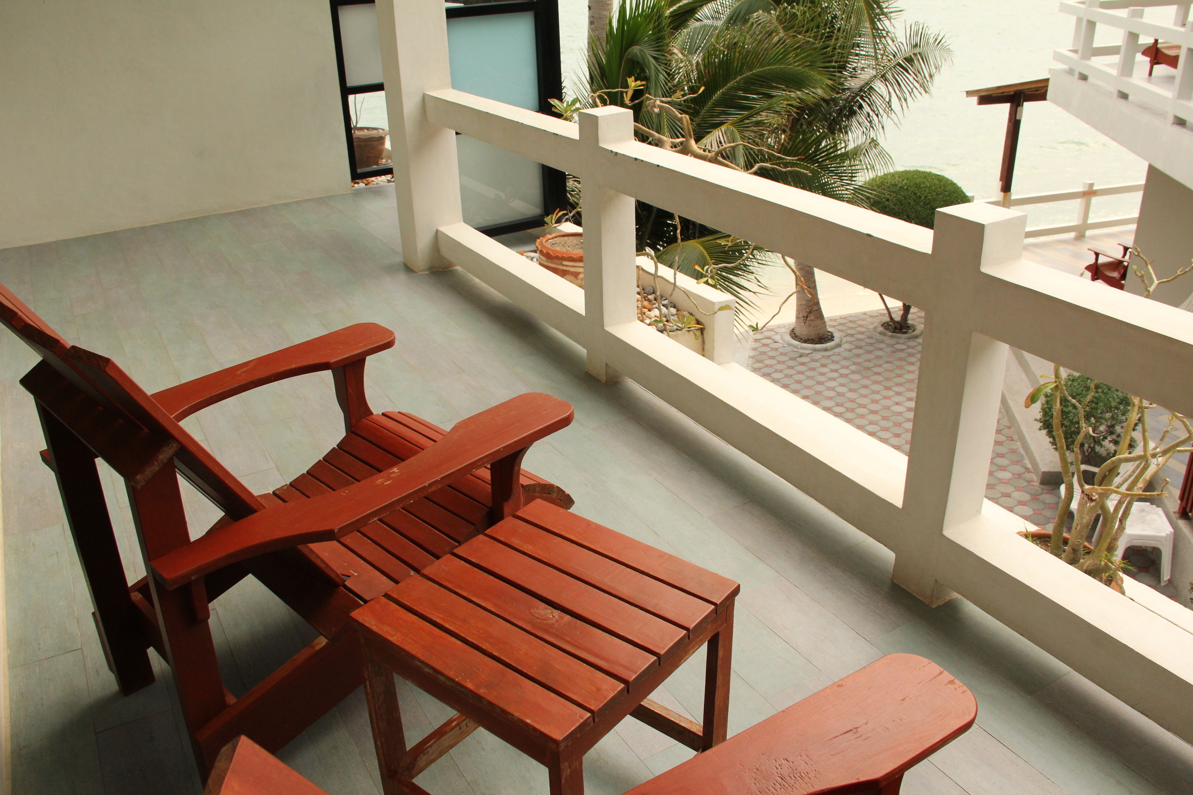 A balcony with wooden furniture and a white railing overlooking a garden.