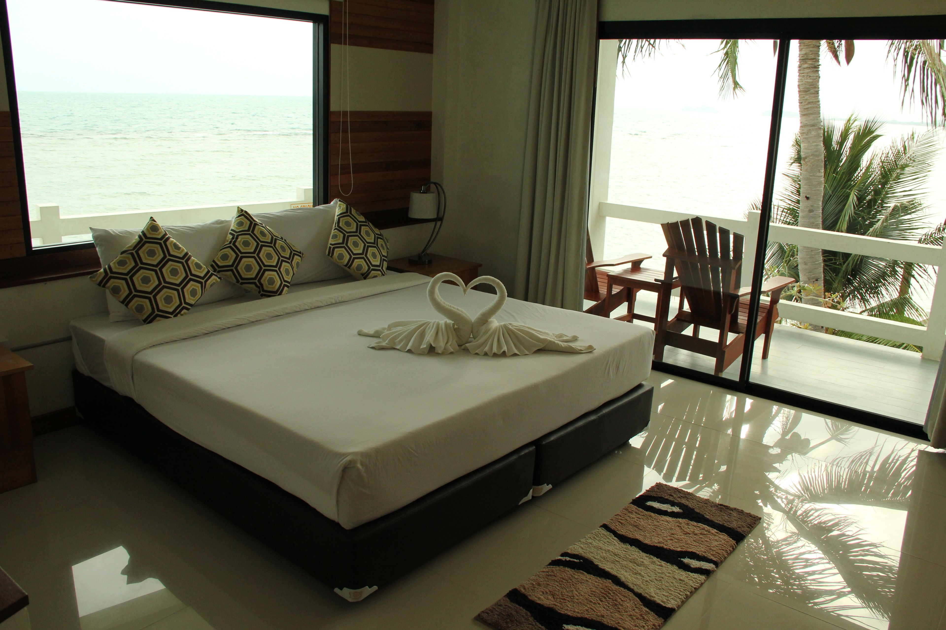 A hotel room with a large bed, a view of the ocean, a balcony with a chair, and a wooden floor.