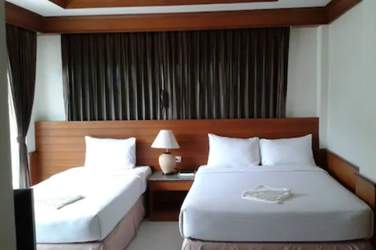 A hotel room with two single beds, a wooden headboard, a nightstand with a lamp, and a curtain backdrop.