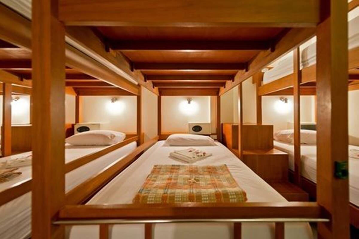 A row of wooden bunk beds with white bedding and a central bed with a patterned blanket.