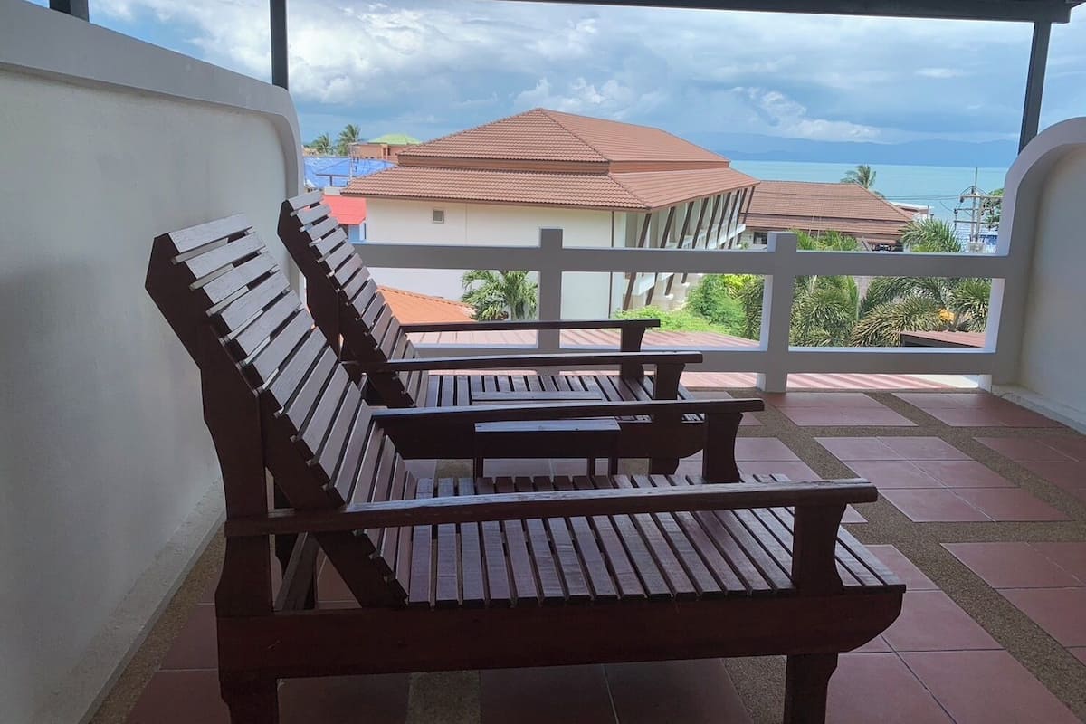 A covered outdoor seating area with wooden benches and a view of buildings and a body of water.