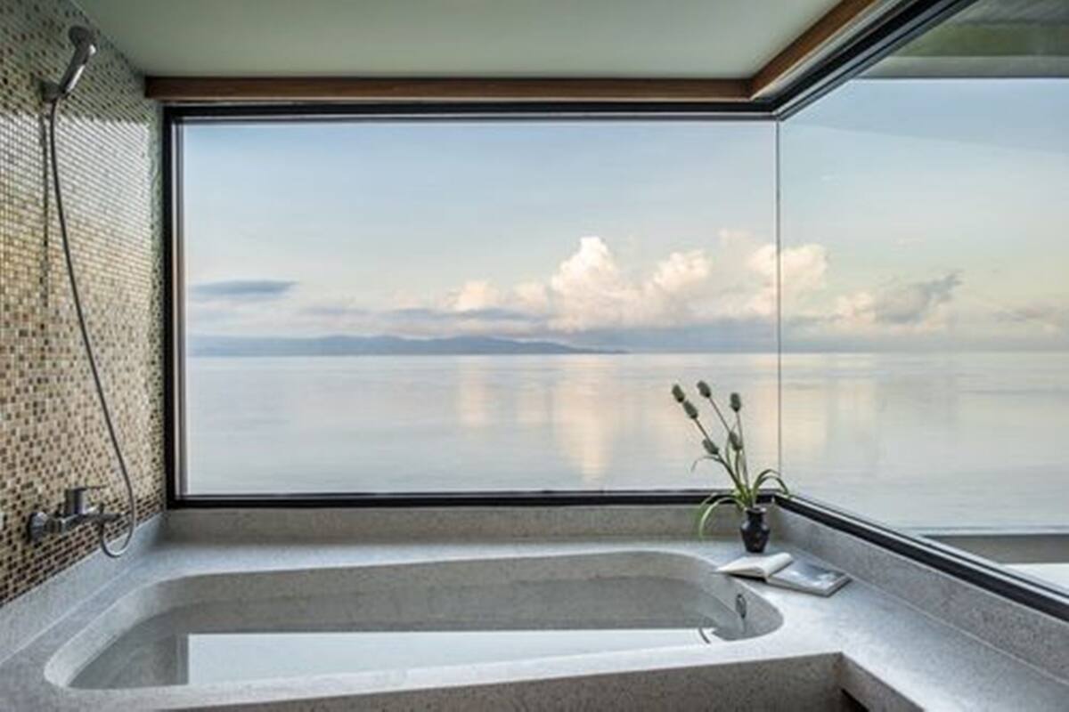 A modern bathroom with a large bathtub, a glass shower enclosure, and a view of the sea.