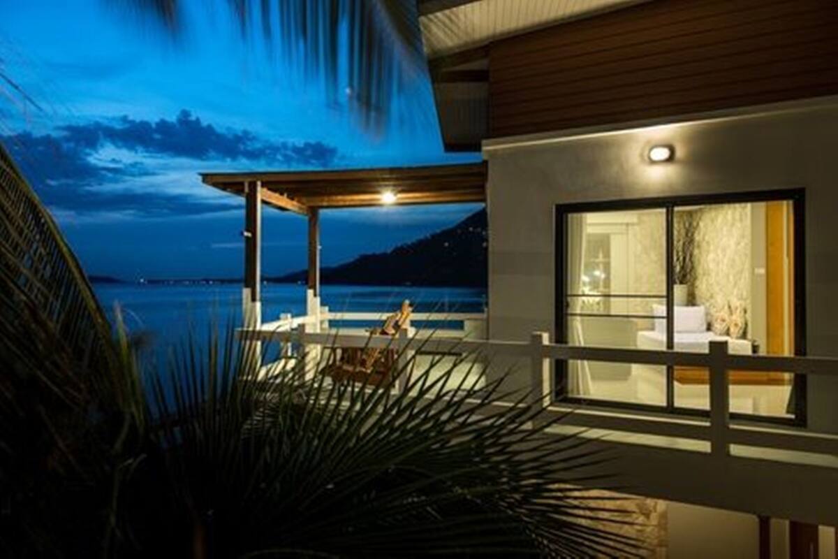 A modern building with a covered outdoor area, a large window, and a view of the sea.