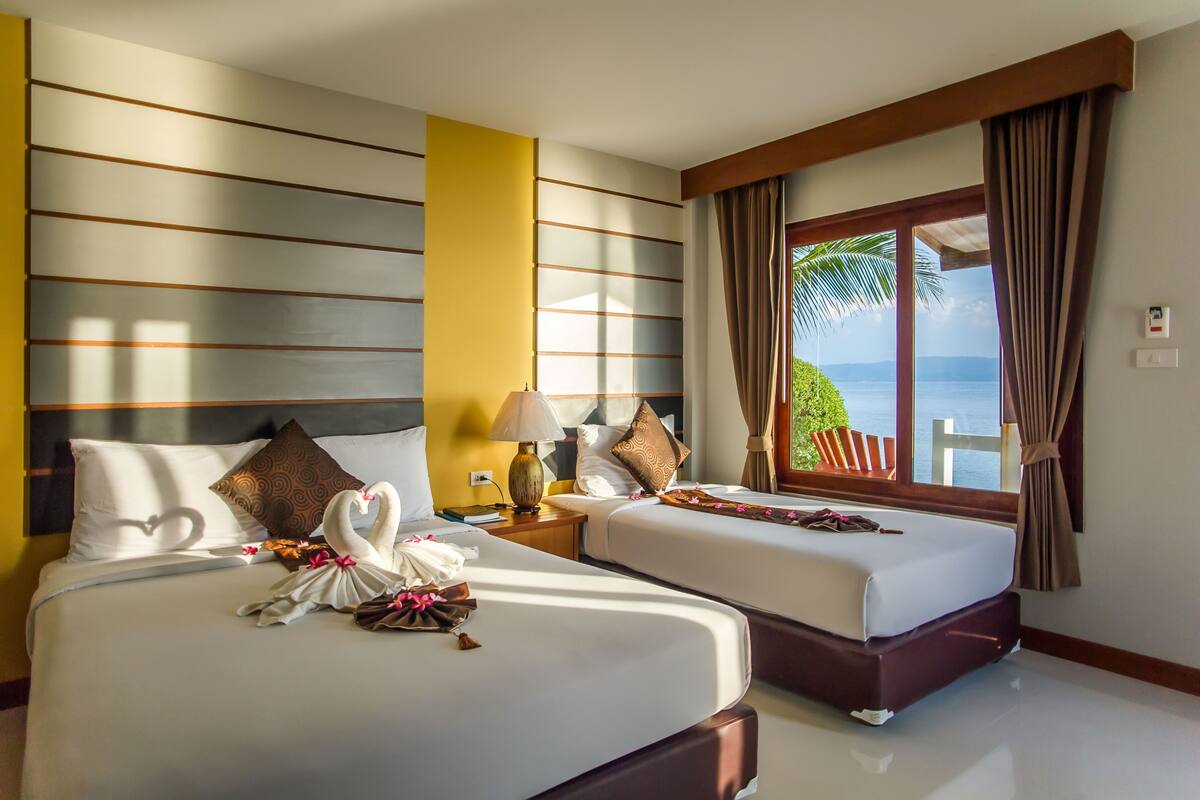 A hotel room with two beds, a view of the sea, and a window with curtains.