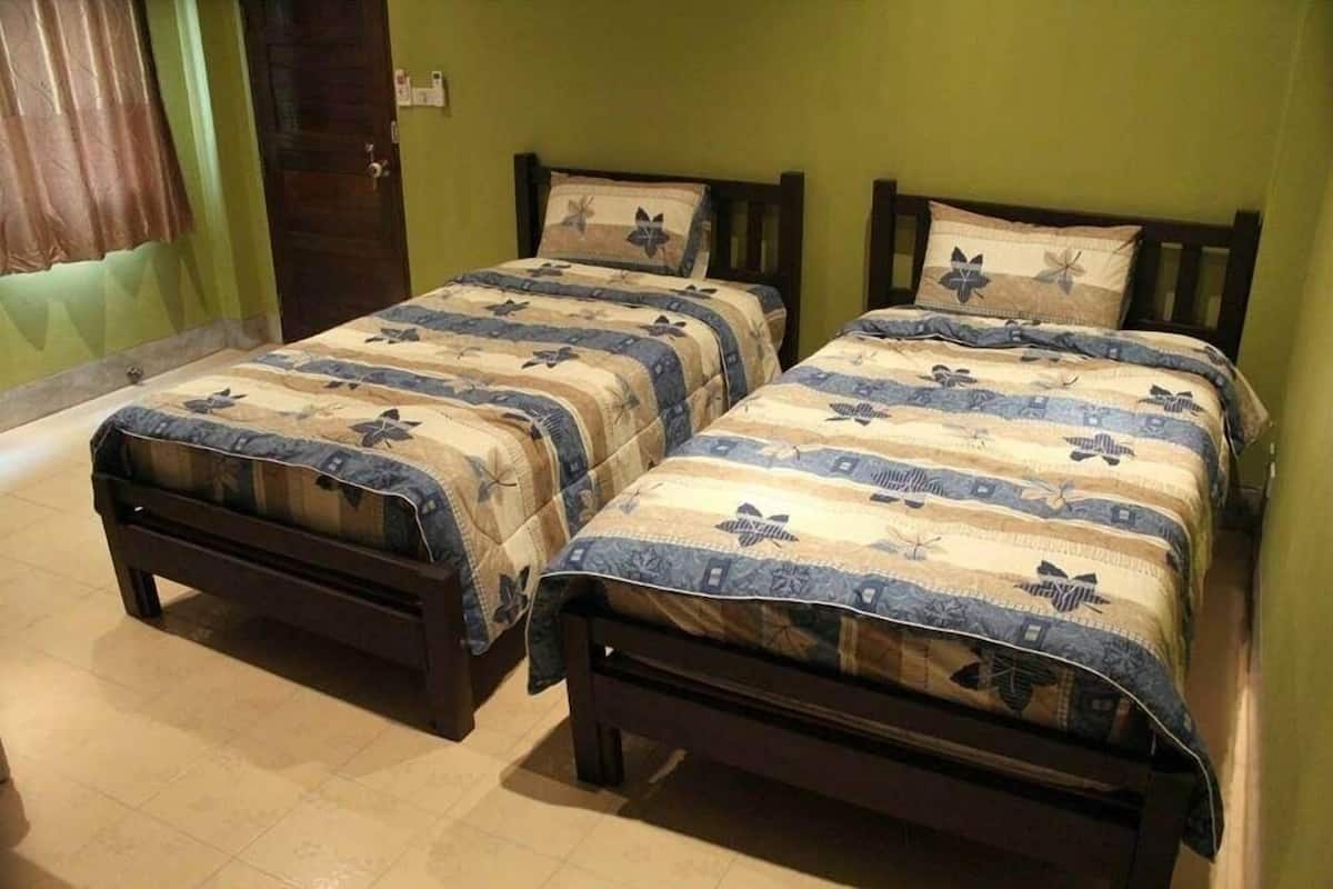 Two twin beds with matching floral-patterned bedding, wooden headboards, and a green wall.