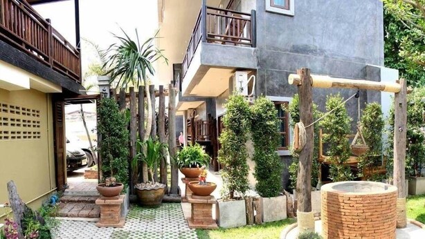 A courtyard with a tiled walkway, potted plants, a brick structure, and a wooden swing set. - PJ House (Chiang Mai)