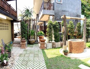 A courtyard with a tiled walkway, potted plants, a brick structure, and a wooden swing set. - PJ House (Chiang Mai)