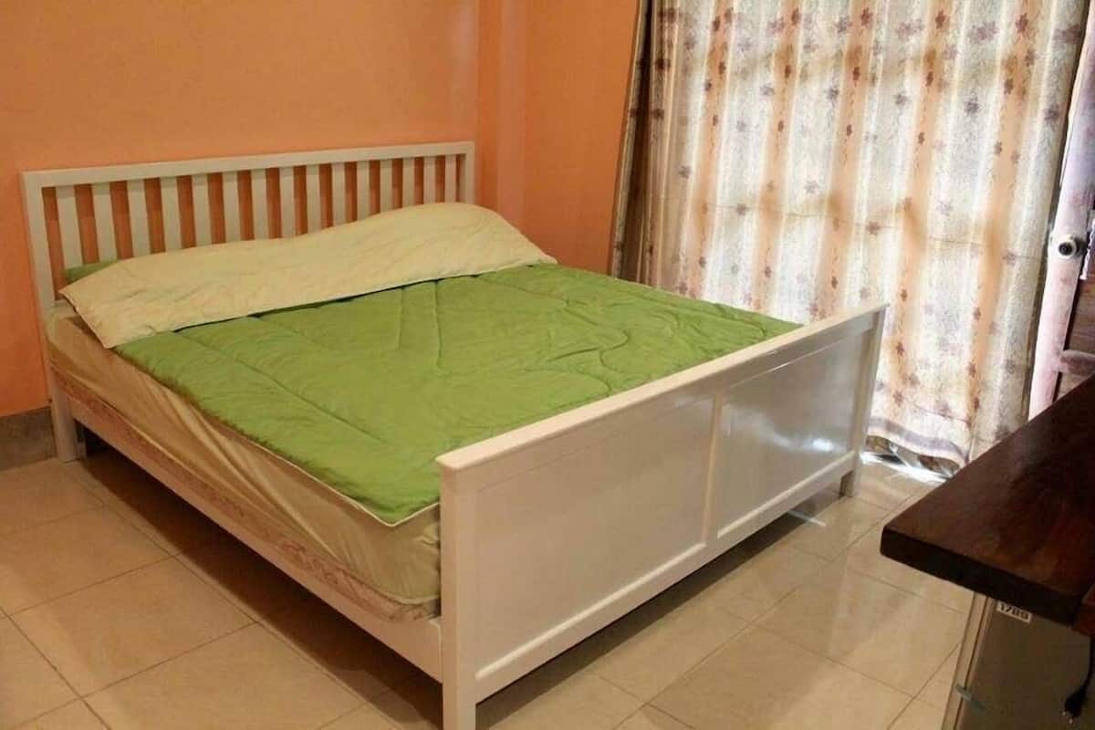 A single bed with a white frame and green bedding in a room with orange walls and a patterned curtain.
