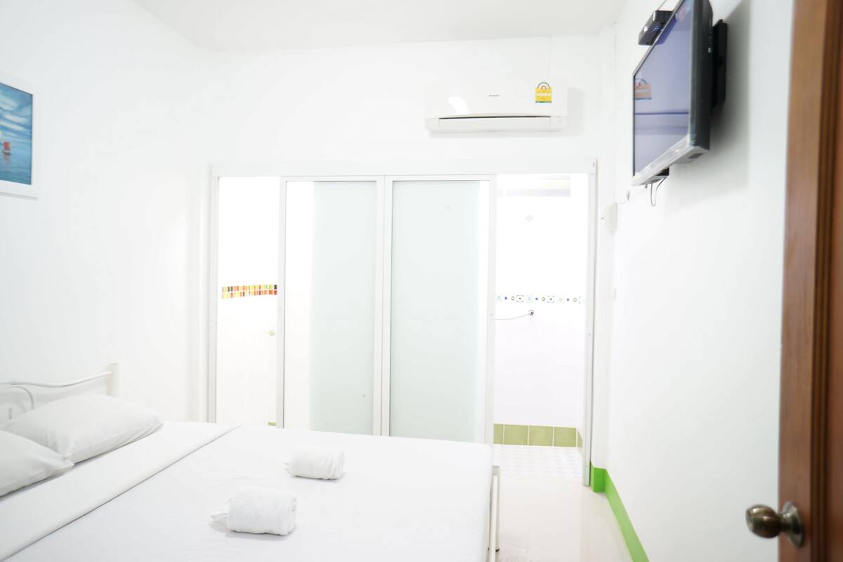 A hotel room with a bed, a TV, an air conditioner, and a sliding door to the outside.