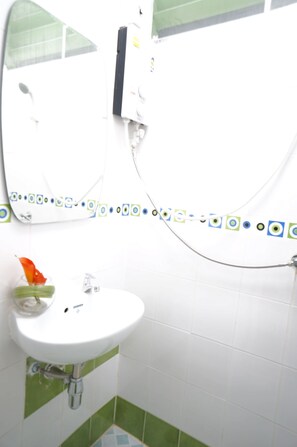 Un baño con un lavabo blanco, baldosas blancas y verdes, un espejo y una zona de ducha.