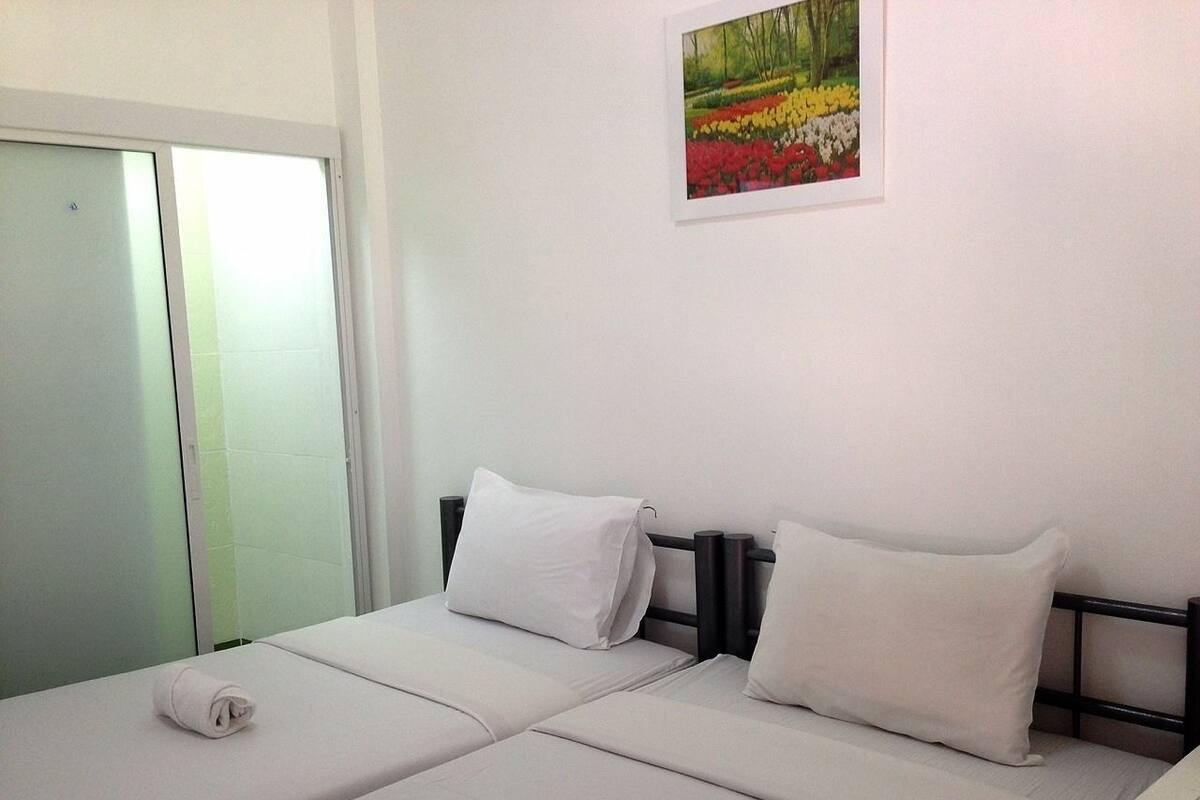 A simple, clean room with two beds, white bedding, and a painting of flowers on the wall.