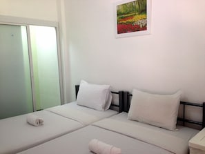 Una habitación sencilla y luminosa con dos camas, ropa de cama blanca y un cuadro de flores en la pared.