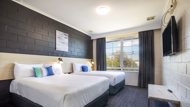 Habitación de hotel con dos camas, televisión y ventana con cortinas.