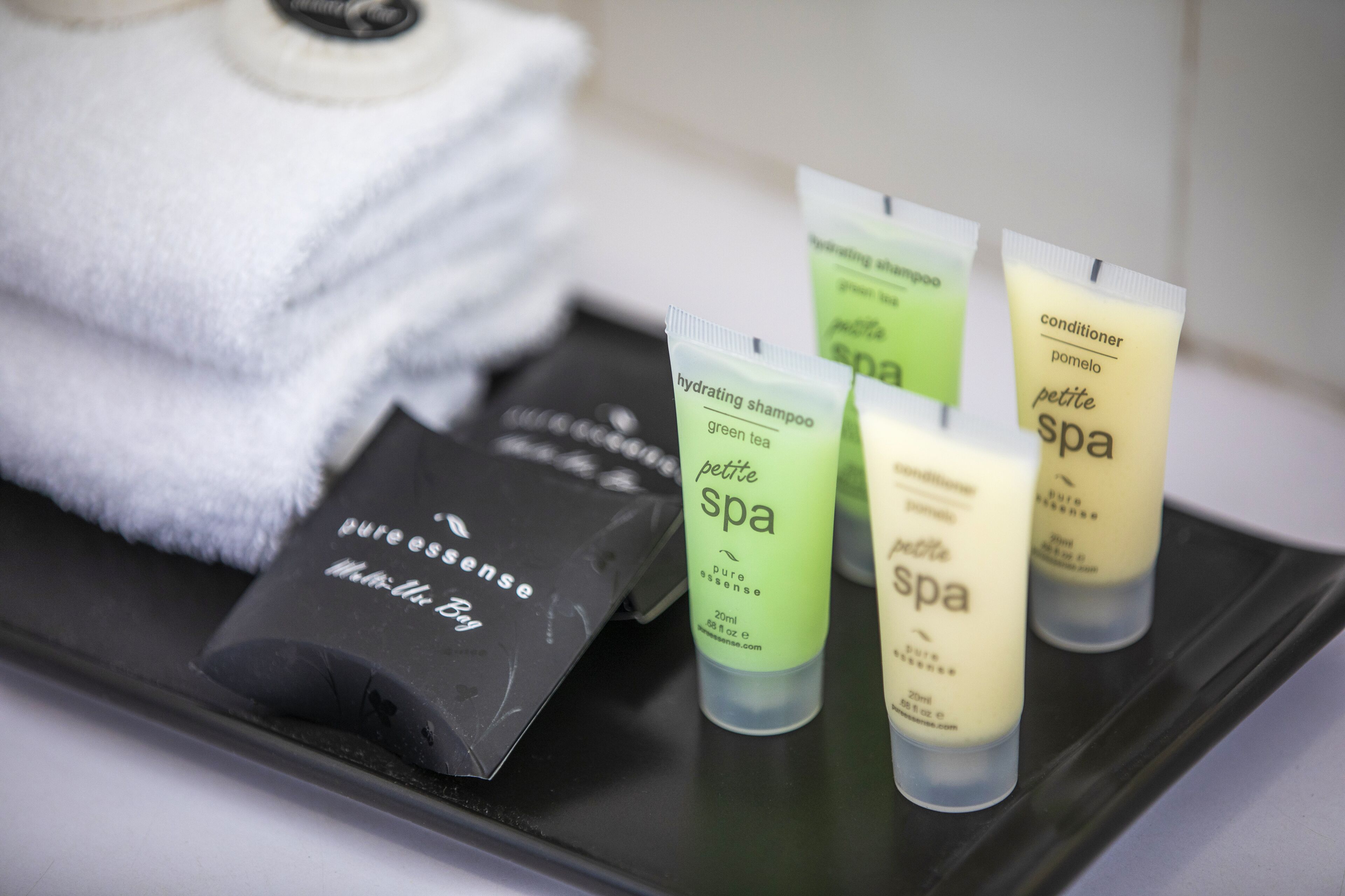 A tray with toiletries including a green tea shampoo, a conditioner, and a black bag labeled "pure essence."