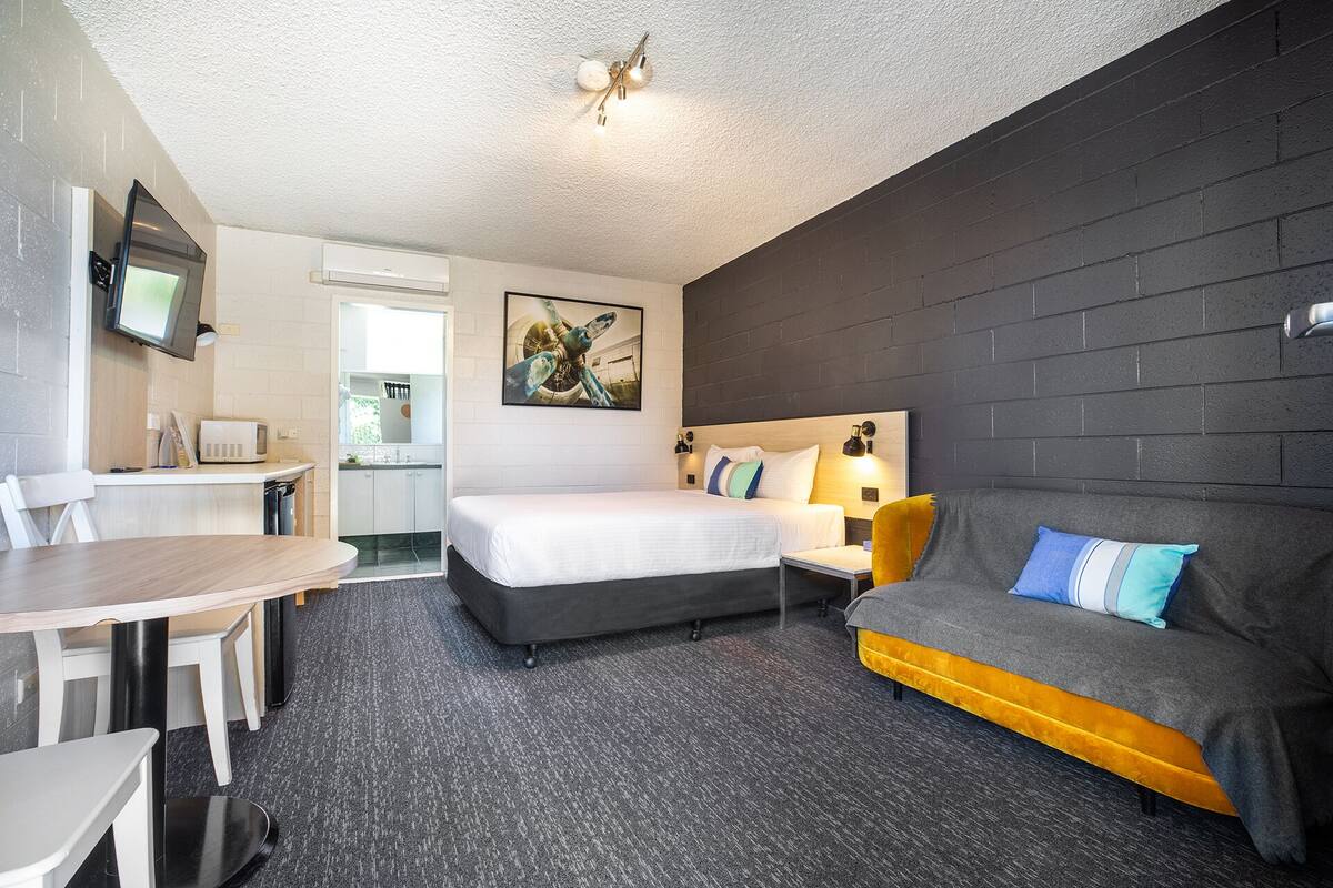 A modern hotel room with a bed, a sofa, a dining area, and a kitchen.