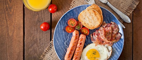Un plato de desayuno con salchichas, tocino, un huevo frito y tomates sobre un plato azul.