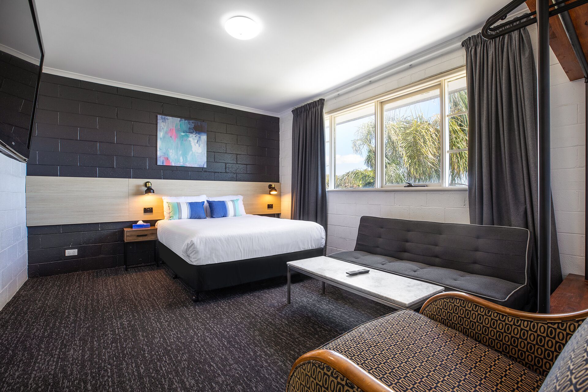 A hotel room with a bed, a sofa, a small table, and a window with curtains.