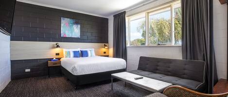 Una habitación de hotel con cama, sofá, una mesita y ventana con cortinas.