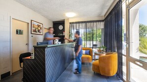 Un hall de hotel con una mesa de recepción, un reloj en la pared y un amplio ventanal con cortinas.