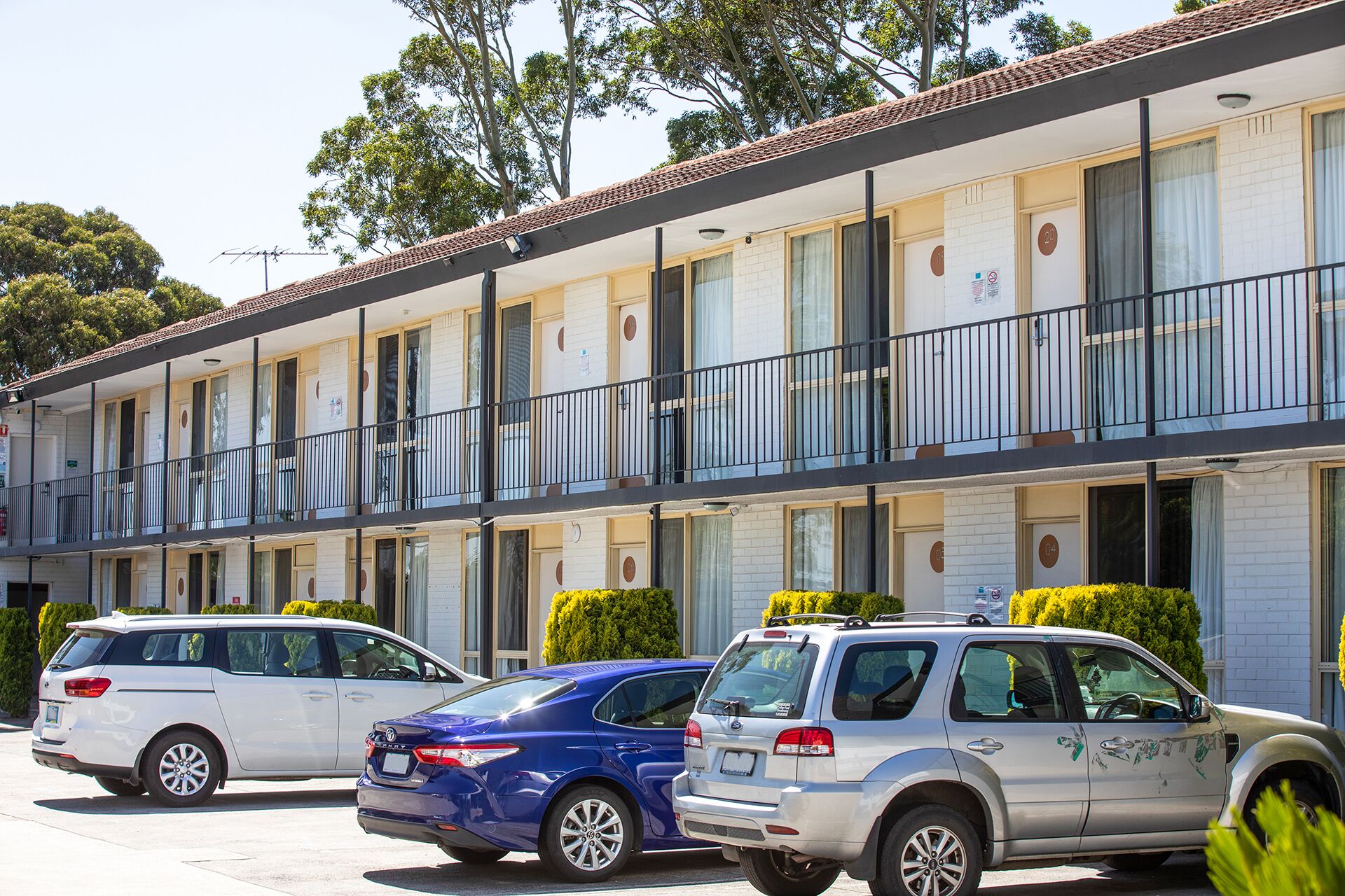 A multi-story motel with a row of rooms, each with a balcony and a window.