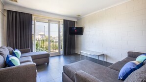 Una sala de estar moderna con sofás grises, un televisor de pantalla plana en la pared y un balcón con cortinas.