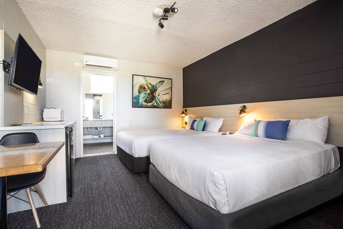A hotel room with two beds, a desk, a TV, and a bathroom visible through an open door.