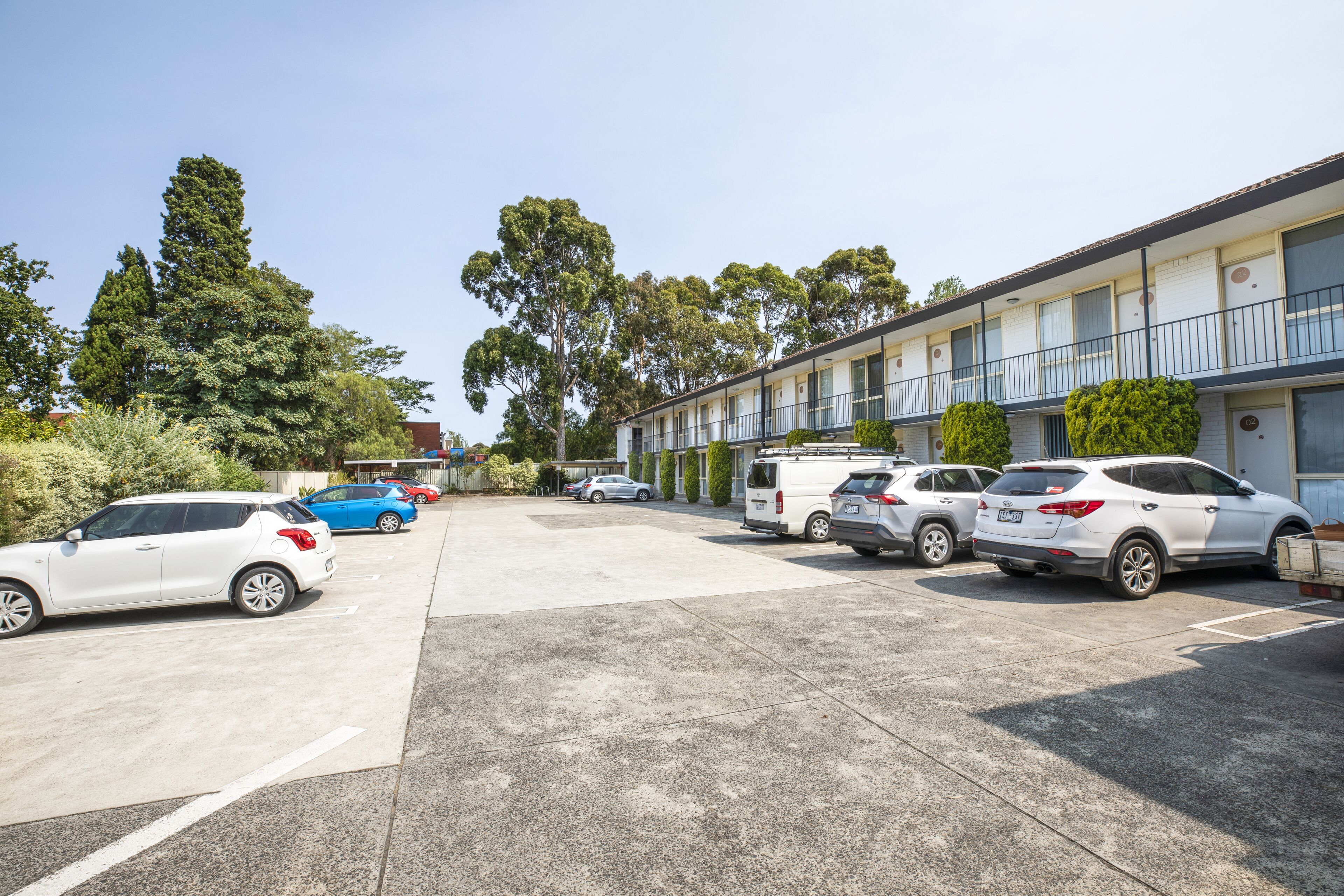 A parking lot with several cars parked in front of a building with multiple balconies.