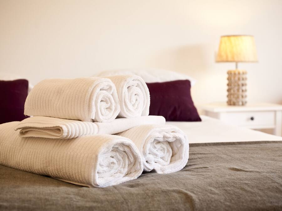 A neatly made bed with rolled white towels and a lamp on a bedside table.