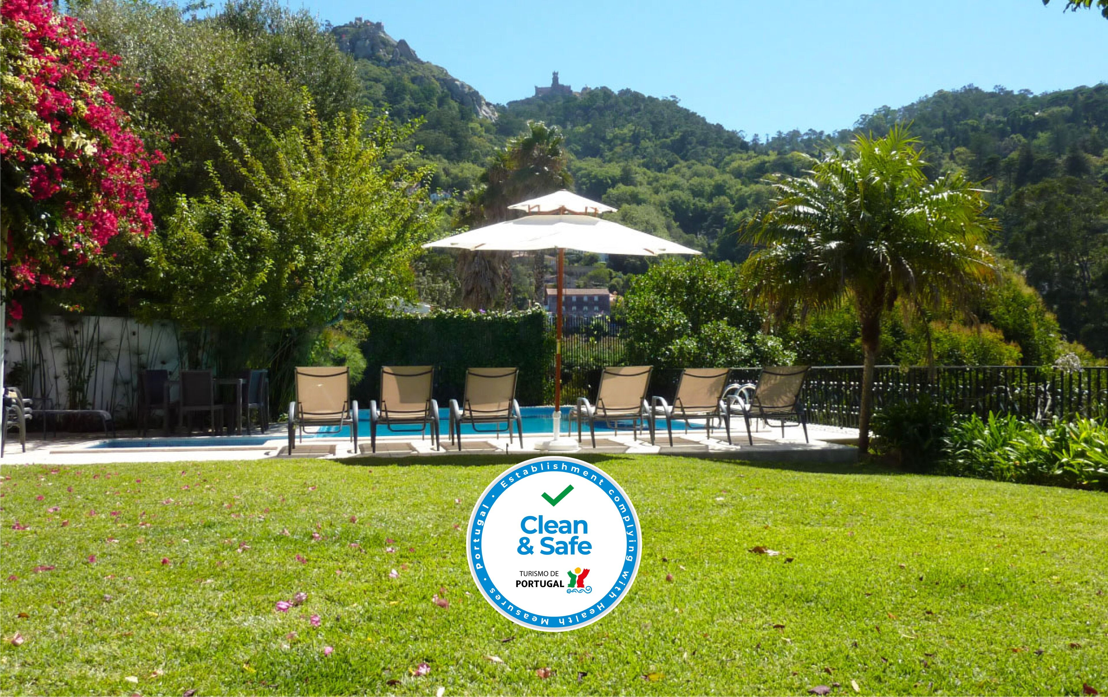 Zona de piscina con sillas de descanso y una sombrilla, rodeada de exuberante vegetación y colinas.