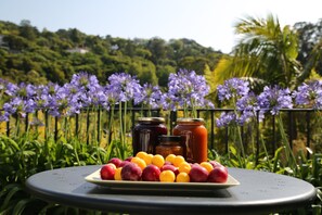 A table with a plate of fruit and jars of preserves, set against a backdrop of purple flowers and greenery.