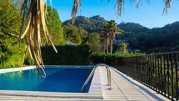 A swimming pool with a metal ladder, surrounded by a tiled deck and a metal fence.