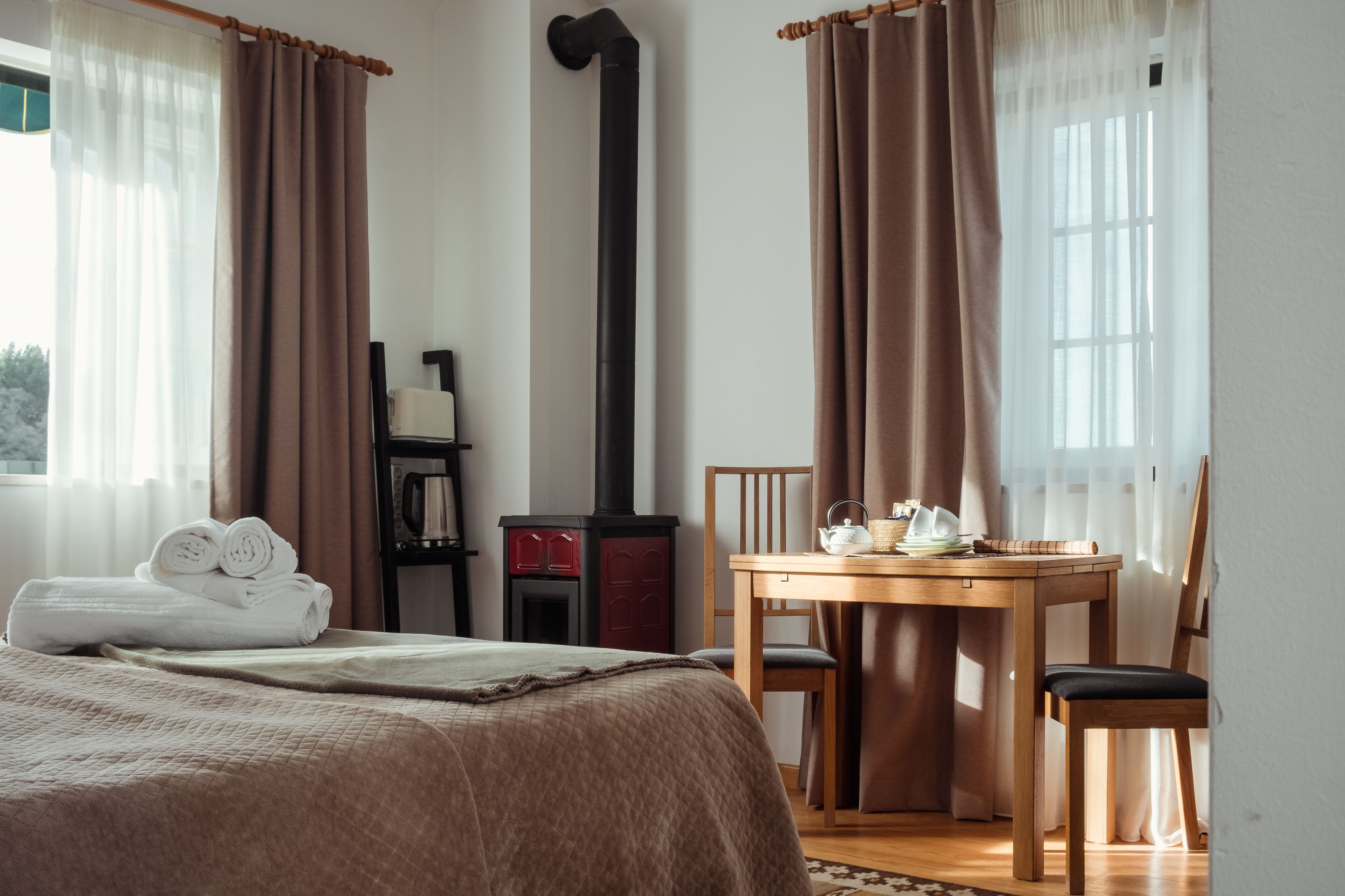 A hotel room with a bed, a table with chairs, a fireplace, and curtains.