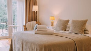 Un dormitorio con una cama grande, una mesita de noche con lámpara, una silla y vistas al exterior.