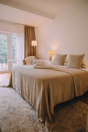 A bedroom with a large bed, a bedside table with a lamp, a chair, and a view of the outdoors.