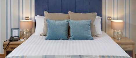 A neatly made bed with striped bedding, two bedside lamps, a telephone, and a small table with a lamp.