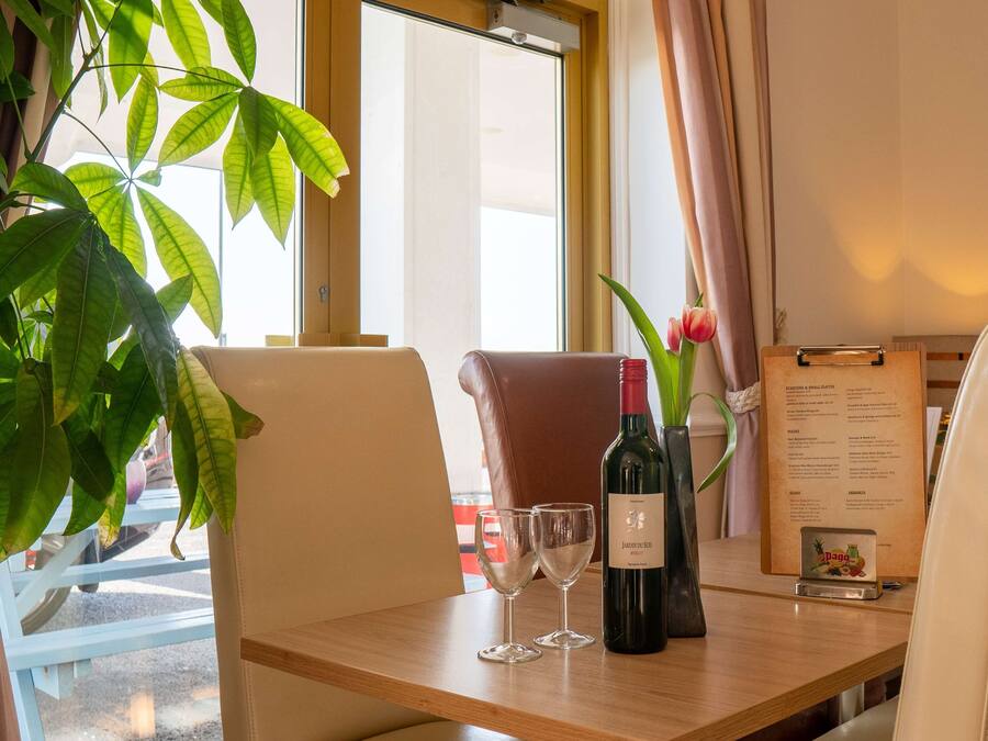 A dining table with two wine glasses, a bottle of wine, and a menu.