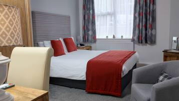 A hotel room with a bed, two nightstands, a lamp, a chair, and a window with curtains.